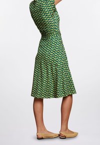 Grön och gul mönstrad klänning med korta ärmar, åtsittande midja, utsvängd kjol och knälång fåll, parat med ljusbeige, vävda ballerina-skor.