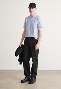 Polo shirt bleu clair avec col, jeans noirs et chaussures noires. Casquette noire portée à l'envers. Tatouage visible sur l'avant-bras. Tenue décontractée.