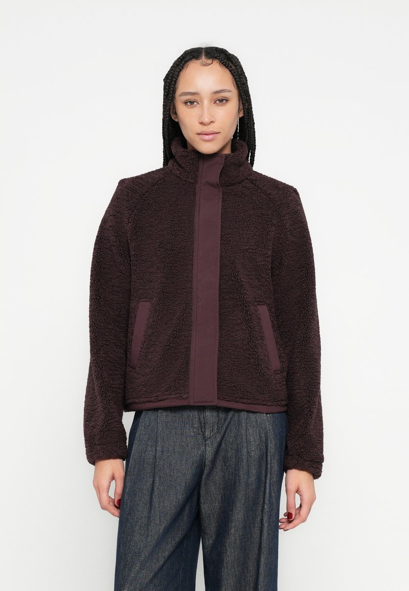 Fleecejacke in dunkelburgunderrot mit hohem Kragen, zwei Seitentaschen und einer glatten mittleren Blende. Strukturierter Stoff sorgt für Wärme und Komfort.