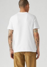 Vit bomulls-T-shirt med klassisk rund hals, korta ärmar och rak fåll, ihop med kordbyxor som har vertikala ribbor.