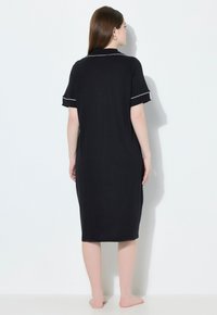 Vestito da notte nero alla lunghezza del ginocchio con maniche corte, bordato di bianco nei polsini e al colletto, realizzato in tessuto morbido e liscio; design minimalista.
