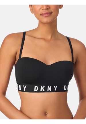 Vrouw draagt een zwarte DKNY bandeau bh met dunne bandjes en een elastische band met merknaam onder de buste, tegen een effen lichte achtergrond.