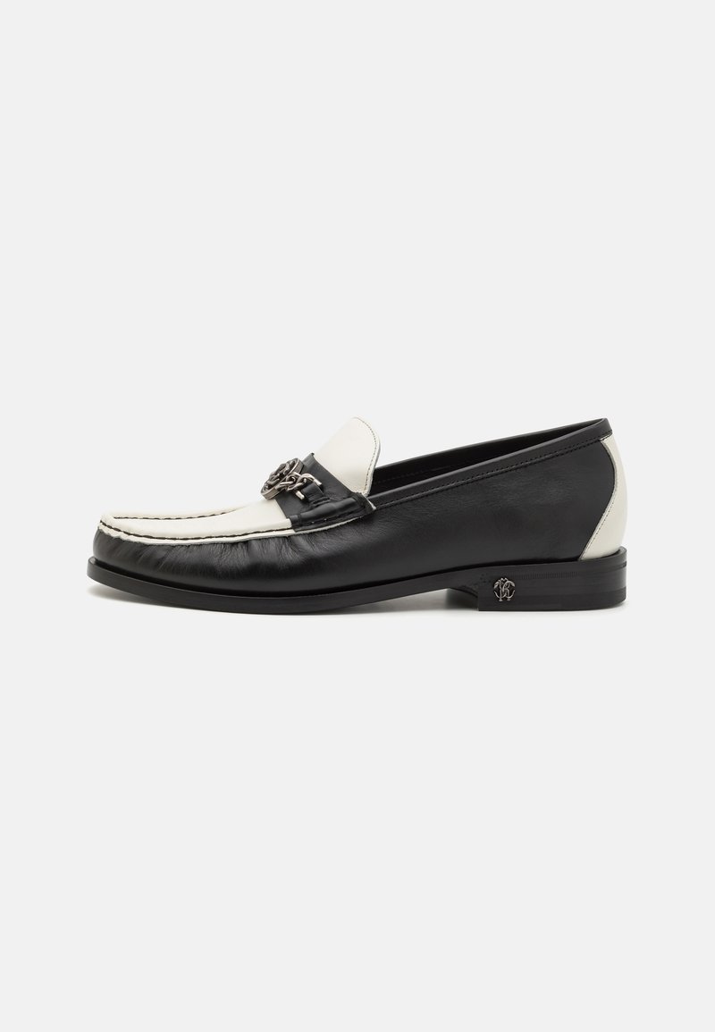 Black and white leather loafers with a rounded toe, contrast stitching, and a decorative metal accent on the front. Flat heel design.
