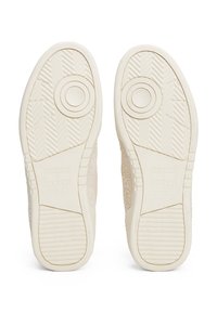 Suelas de zapatos de goma beige texturizada, con acentos circulares y un logo. Cuerpo del zapato hecho de un material suave y de color claro con un diseño minimalista.