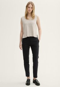 Flødefarvet ribstrikket ærmeløs top med V-udskæring og cropped kant, kombineret med slim-fit sorte bukser og sorte loafers.