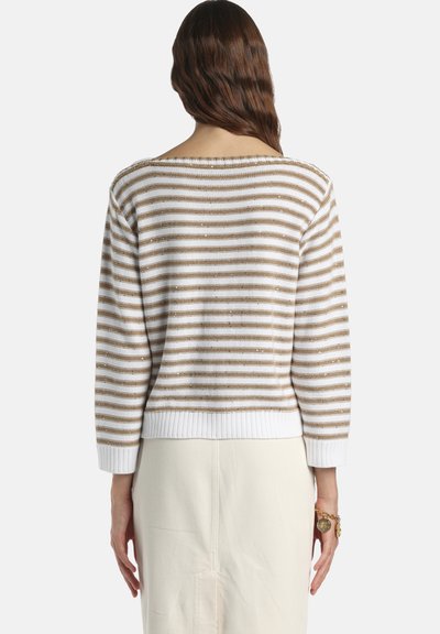 Femme aux longs cheveux bruns portant un pull rayé blanc et beige et une jupe crème, vue de dos sur un fond blanc.