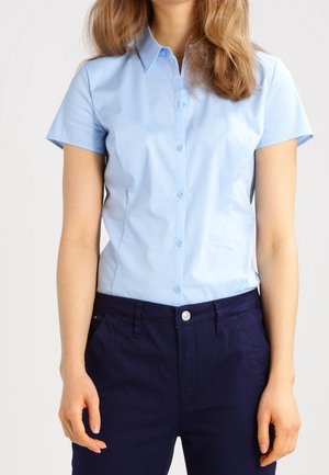 Camicetta azzurro chiaro a maniche corte con chiusura a bottoni, colletto e texture liscia, abbinata a pantaloni blu scuro con tasche frontali.