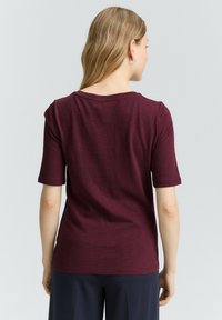 Bordeaux top met korte mouwen, een ontspannen pasvorm, ronde halslijn en zachte textuur, met een achterkant die een lichte drapingdetail heeft.