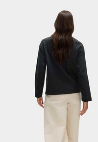 Ciemnoszara, długorękawowa bluzka o luźnym kroju. Posiada okrągły dekolt i teksturowany materiał, zestawiona z jasnobeżowymi spodniami typu wide-leg.