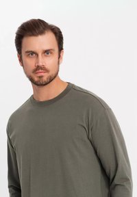 T-shirt a maniche lunghe verde oliva realizzato in tessuto morbido con scollatura a girocollo e vestibilità rilassata. Presenta dettagli cuciti sulle spalle.