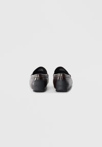 Brown leather loafers with a low block heel, featuring black accents along the opening and embossed logo on the back heel. Smooth texture.