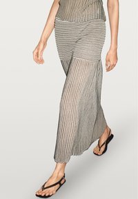 Maxikjole med lodrette sorte og hvide striber, gennemsigtigt stof og tætsiddende overdel, kombineret med sorte flip-flops.