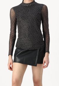 Maglietta nera in rete a maniche lunghe con un delicato motivo a leopardo, abbinata a una minigonna in pelle nera aderente con uno spacco frontale.