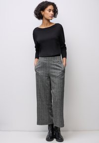 Musta neule, jossa on leveä kaula-aukko, yhdistettynä harmaisiin kuvioituihin väljätaskuhousuihin. Mustat nilkkurit viimeistelevät asun.