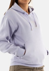 Felpa lavanda realizzata in tessuto morbido, con tasca a marsupio, cappuccio con cordoncino e dettaglio ricamato sul davanti. Texture liscia, vestibilità comoda.