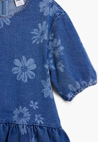 Denimkjole i en blå nuance med lyseblå blomsterprint. Har korte pufærmer og en rynket nederdel ved kanten.