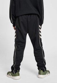Los pantalones de chándal negros cuentan con franjas laterales blancas y un ajuste relajado. Se combinan con zapatillas texturizadas verdes y blancas.