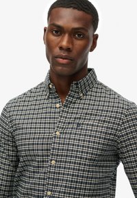Camisa de cuadros en color navy y blanco, hecha de algodón, con cuello, bolsillo en el pecho y cierre clásico de botones.