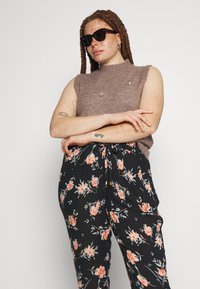 Top tricot fără mâneci, de culoare marron, cu broderie florală, asortat cu pantaloni negri cu un imprimeu floral în nuanțe de roz, portocalie și verde.