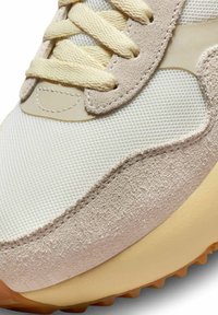 Sneaker con una parte superiore in suede beige testurizzato e mesh bianco, con lacci crema e una suola in gomma color taupe. Dettaglio di cucitura evidente.