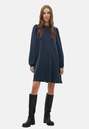 Marineblaues langärmliges Kleid mit entspannter Passform, Puff-Schultern und weichem Stoff, kombiniert mit knielangen schwarzen Lederstiefeln.