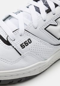 White sneaker made of leather and mesh, featuring perforations, black accents, and a prominent "550" on the side. Textured sole.