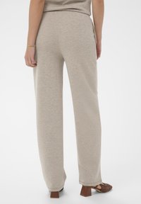 Svetlo béžové lounge nohavice z mäkkej látky s širokým strihom a bočnými vreckami, doplnené hnedými sandálmi na podpätku z tkaného materiálu.