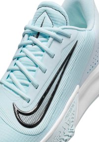 Lysblå atletisk sneakers med en tekstureret overdel, sort Swoosh-logo, flade snørebånd og en hvid ydersål med skrid- og vægmønster.