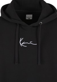 Čierna mikina s kapucňou a šnúrkami, s bielym vyšívaným logom na hrudi. Mäkkučká bavlnená látka, klokanie vrecko a klasický dizajn.