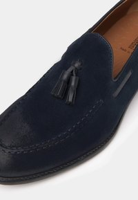 Mocassini in suede blu navy con doppie frange in pelle, dettagli cuciti e una finitura liscia. Il design include una silhouette classica slip-on.