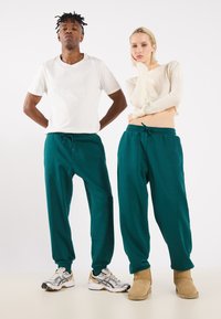 Teal joggers with elastic waistband and drawstring, paired with a white T-shirt and a ribbed beige crop top, worn with sneakers and boots.