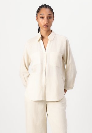 Lys beige, langermet skjorte med knapper laget av lin, med to frontlommer og krage, med buet nederkant.