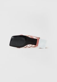 Pink strappy sandal with a square black sole. The heel features a smooth texture and an attached label with blank white section for details.