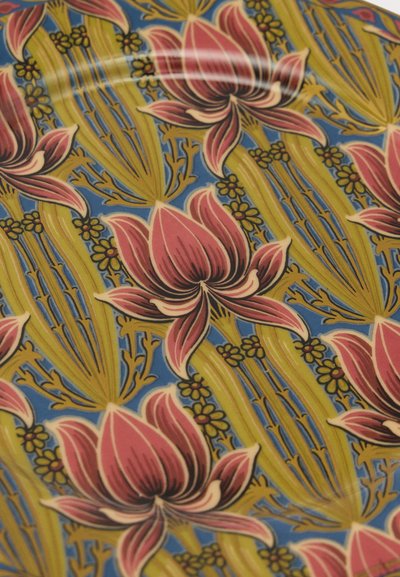 Assiette en céramique à motif avec de grandes fleurs de lotus roses, des tiges vertes et de petites fleurs jaunes sur fond bleu.