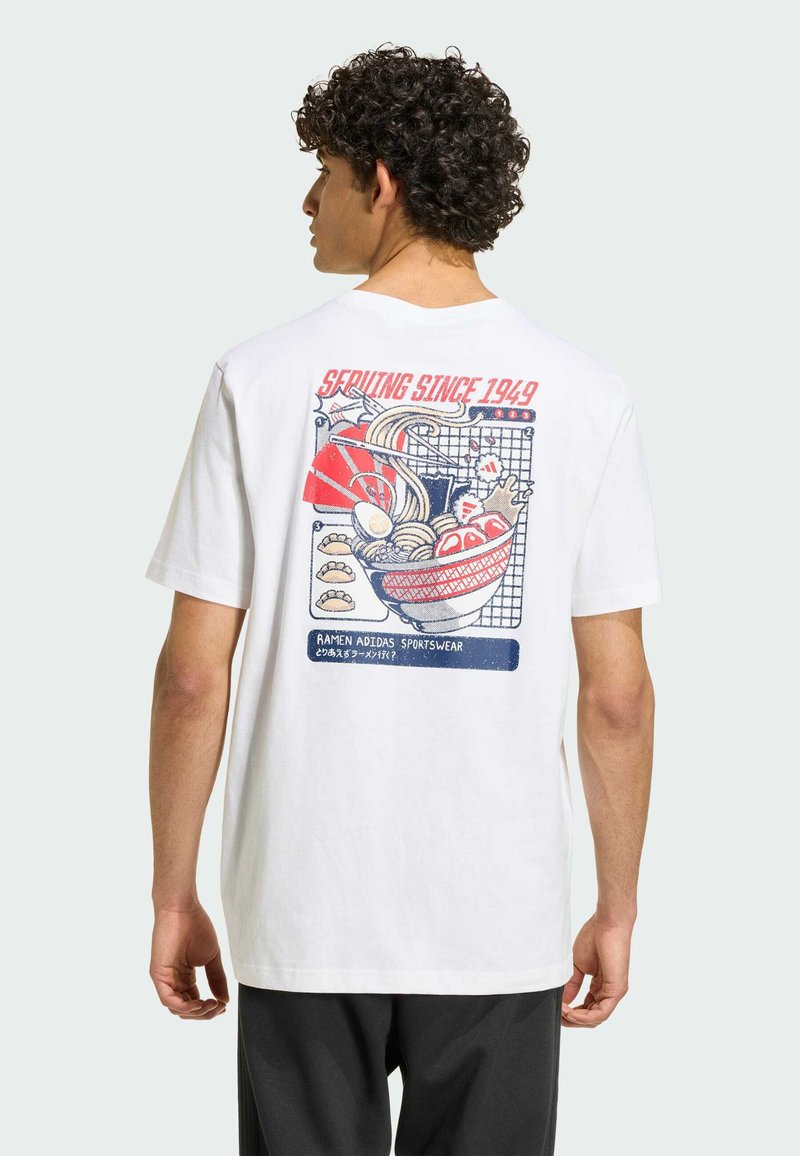 Homme aux cheveux bouclés portant un t-shirt blanc avec un motif coloré d’un bol de ramen et un texte rouge « Serving Since 1949 » au dos.