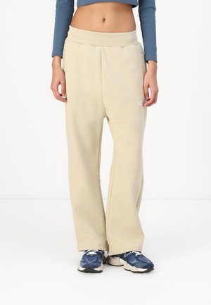 Beige vide bukser med ribbet liv, myk tekstur og sidelommer. Kombinert med blå joggesko med hvite detaljer.