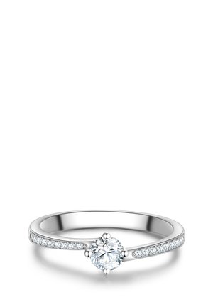Anello di fidanzamento in argento con un diamante centrale rotondo e diamanti più piccoli incastonati lungo la fascia su sfondo bianco.