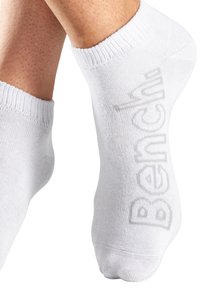 White ankle socks made of a smooth, lightweight fabric with a ribbed cuff, featuring a light gray "Bench" logo on the side.