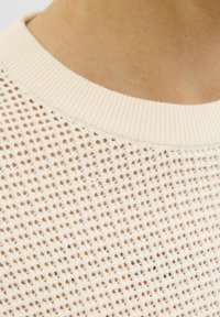 Lekki sweter z dzianiny z luźnym, otwartym splotem w kolorze kremowym, z prążkowanym okrągłym dekoltem. Tekstura jest miękka i przewiewna.