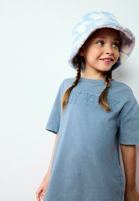 Ljusblå bomull t-shirt med korta ärmar, med präglad text "NEW YORK". Matchad med en fluffig, mönstrad blå och vit bucket hat.