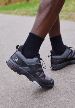 Zapatillas de senderismo Salomon X Ultra GTX en negro y gris, con una parte superior texturizada, puntera reforzada y suela con patrón y detalles en rojo.