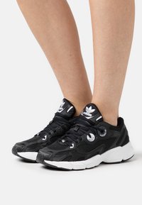 Sorte atletiske sneakers med mesh-overdel, hvide accenter og runde snørehuller. Tykk hvid mellemsål, gummiydersål og polstret krave for komfort.