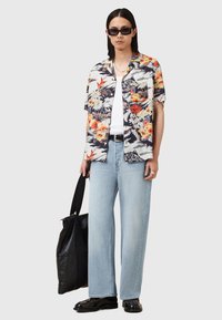 Camicia a maniche corte con stampa floreale in navy, bianco e arancione, abbinata a jeans ampi in denim chiaro. Borsa a tracolla nera in pelle e scarpe.