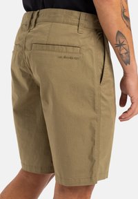 Shorts khaki en tissu léger, dotés de poches arrière et d'un logo discret. Texture lisse avec une coupe droite et classique.