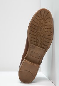 Brązowe skórzane buty z teksturowaną gumową podeszwą; charakteryzują się wzorem w zygzak oraz prostokątnymi wycięciami, zaprojektowane dla lepszej przyczepności i trwałości.