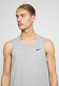 Canottiera in cotone grigia con scollo rotondo, design senza maniche e un piccolo logo Nike nero sul lato sinistro del petto.