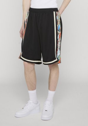 Man wearing black athletic shorts with multicolor side panels, paired with white crew socks and white sneakers, standing against a gray background.