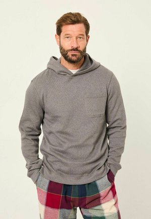 Graue Kapuzenjacke mit einer Fronttasche, langen Ärmeln und einer lockeren Passform, kombiniert mit mehrfarbigen Karo-Hosen in Rot, Blau und Creme.