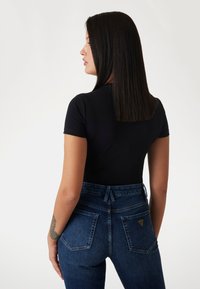 Sort kortærmet top parret med højtaljede blå denim jeans, der har to baglommer og et lille logo mærke på den højre lomme.