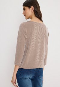 Ljust brunt ribbat linne med bred halsringning och trekvartslånga ärmar, ihop med blå denimjeans. Slät textur och avslappnad passform.
